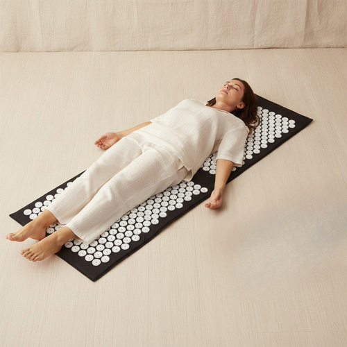 Woman lying on Napio Pressure Mat on floor, eyes closed, relaxed